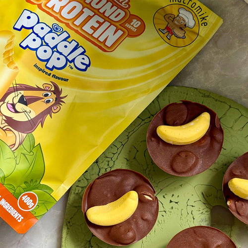 A bag of Paddle Pop Almond Protein biscuits with banana-shaped centers, shown next to a bag of protein.