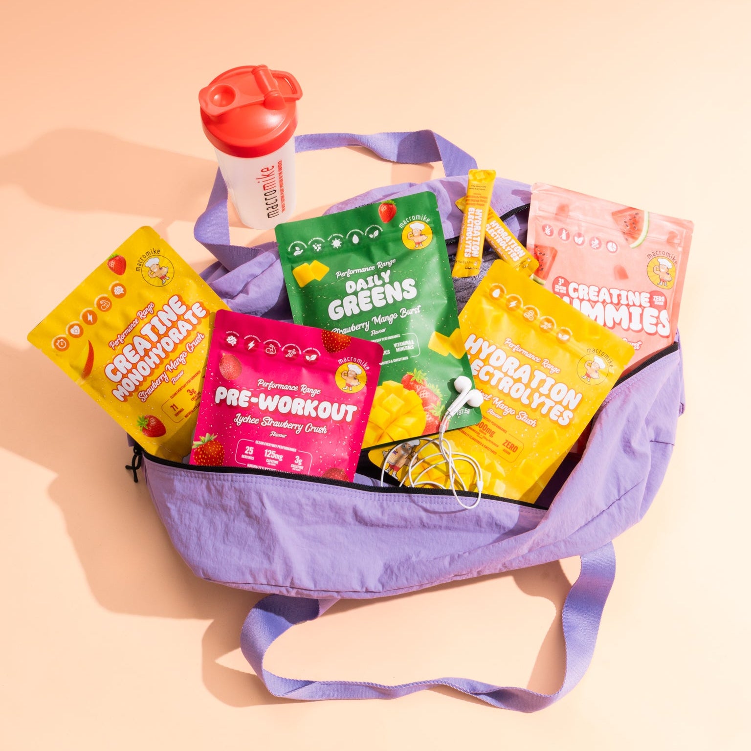 A purple tote bag filled with colorful packaged snacks and drinks, including packets labeled Creatine Powder, Pre-Workout, Daily Greens, and Hydration Electrolytes, on a peach background.